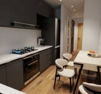 The kitchen of a 3-room apartment with a stove, a dining table, and a floor with a wood decor.