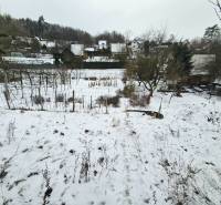 A snowy garden in Lieskovec in Dubnica nad Váhom with cottages and trees in the background.