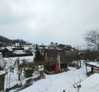 A snow-covered cottage in Lieskovec in Dubnica nad Váhom surrounded by trees and other cottages.