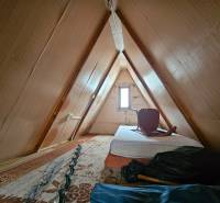 Attic of a cottage with a mattress and a chair, wooden decor, light walls.