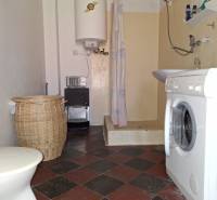 A bathroom in a family house with a washing machine, shower, boiler, and tiles.