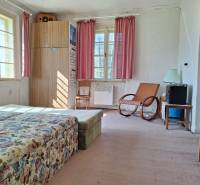 A room with a floral sofa, an armchair, a wardrobe, and pink curtains in a family house.