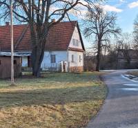 A family house in Orávka with a red roof, a large tree, and a winding road.