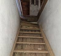 An old wooden staircase leads to the attic of a family house with a trapezoidal roof.