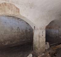 A stone cellar space in a family house with brick vaults and peeling plaster.