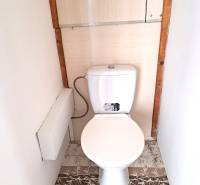 A toilet with a white flush and a floor with a wooden decor in a 4-room apartment.