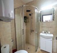 A bathroom in a holiday apartment with a corner shower, sink, and mirror in a decorative frame.