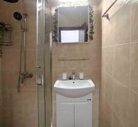 Bathroom in a holiday apartment with a shower and a sink, tiled with light tiles.