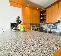 A kitchen in a 2-room apartment with a wooden decor and a fruit bowl on a stone countertop.