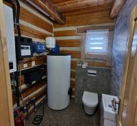 A bathroom in a cabin with a toilet, sink, and technical equipment. The interior is dominated by wood.