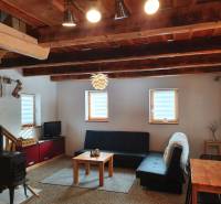 The interior of a cottage with a tiled stove, a sofa, and a wooden ceiling made of solid beams.