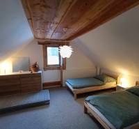 The attic of the cottage with two beds and a chest of drawers with a wooden decor.