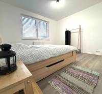 Bedroom in a 3-room apartment with wood-patterned flooring, a bed, and a nightstand.