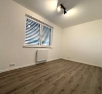A room with a wooden decor floor in a 3-room apartment, white walls, and a radiator.