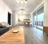 Living room with wood-patterned flooring and a dining table in a three-room apartment.