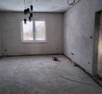 Room of an unfinished family house, bare walls, large window, concrete floor, hanging lights.
