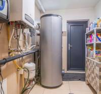 Technical room in a family house with a boiler, tank, and shelves with cleaning products.