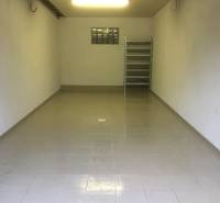 A view into an empty garage with gray tiles on the floor and a shelf in the back.