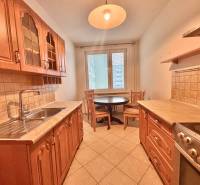 A kitchen in a 3-room apartment with brown cabinets, a dining table, and light tiles.