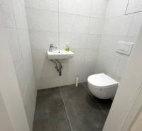 A small bathroom in a 2-room apartment with a toilet, sink, and gray tiles.