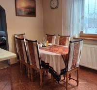 Dining table with six chairs, curtains, and decorative fruit in a family house.