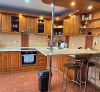 A kitchen in a family house with a wooden decor, equipped with appliances and a bar counter.