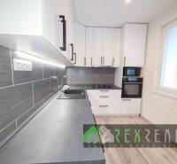 A kitchen in a 3-room apartment with white cabinets, a gray countertop, and a floor with a wooden decor.