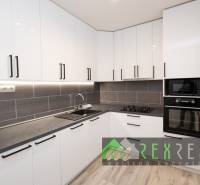 A kitchen in a 3-room apartment with white cabinets and appliances, and a wooden decor floor.