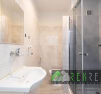 Bathroom in a 3-room apartment with a shower, sink, and light tiles.
