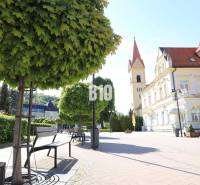 A sidewalk with benches and a historical building in Trenčianske Teplice, plots - housing.