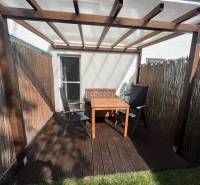 A garden terrace with a wooden table and chairs is covered by a pergola.