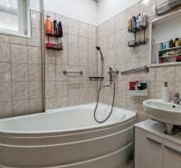 A bathroom in a family house with a corner bathtub, a sink, and white tiles.