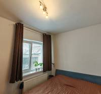 Bedroom in a family house, with a bed, shelves, and a window with a decorative plant.
