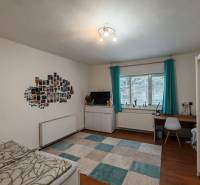 A room in a family house with a desk, a bed, photos on the wall, and a floor with a wooden decor.