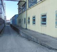 Narrow road and warehouses on Coburgova Street in Trnava with windows secured by bars.