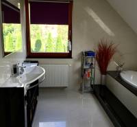 A bathroom in a family house with a bathtub, sink, shelf, and a window with a purple blind.