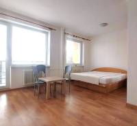 A studio apartment with a bed, table, chairs, and a wooden decor floor.