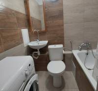 Bathroom in a studio apartment with a bathtub, sink, and washing machine, tiled with ceramic tiles.