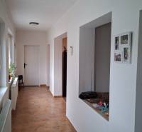 A hallway of a family house with tiles and white walls, with an open door on the right side.