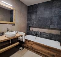 A bathroom in a 2-room apartment with a bathtub, a mirror, and a sink on a wooden table.