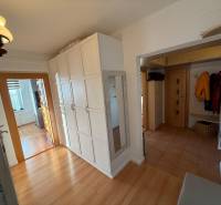A hallway in a 3-room apartment with a wooden decor floor, white cabinets, and a mirror.