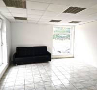 A room with a black sofa, light walls, tiles, and large windows in a building.