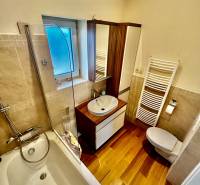 A bathroom with a shower over the bathtub, a sink, and a floor with a wooden decor in a 4-room apartment.