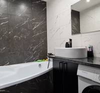 A bathroom with a bathtub, sink, and washing machine in a 2-room apartment, tiled with dark marble tiles.
