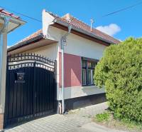 A family house in Nové Zámky with a metal gate and a window, next to lush greenery.