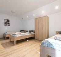 A bedroom in a one-room apartment with three single beds, a wooden decor floor, and a wardrobe.