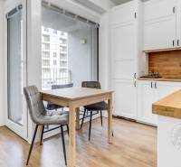 A kitchen with a wooden decor floor, a dining table, and white cabinets in a studio apartment.