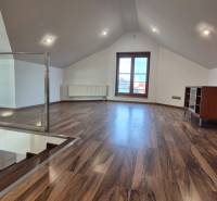 Attic room with wood-patterned flooring, staircase, and large window.