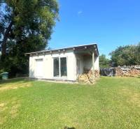 A family house in Melčice-Lieskové with a woodpile and a grassy yard surrounded by trees.