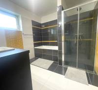 A bathroom in a family house with a bathtub, shower, and window, black and white tiles.